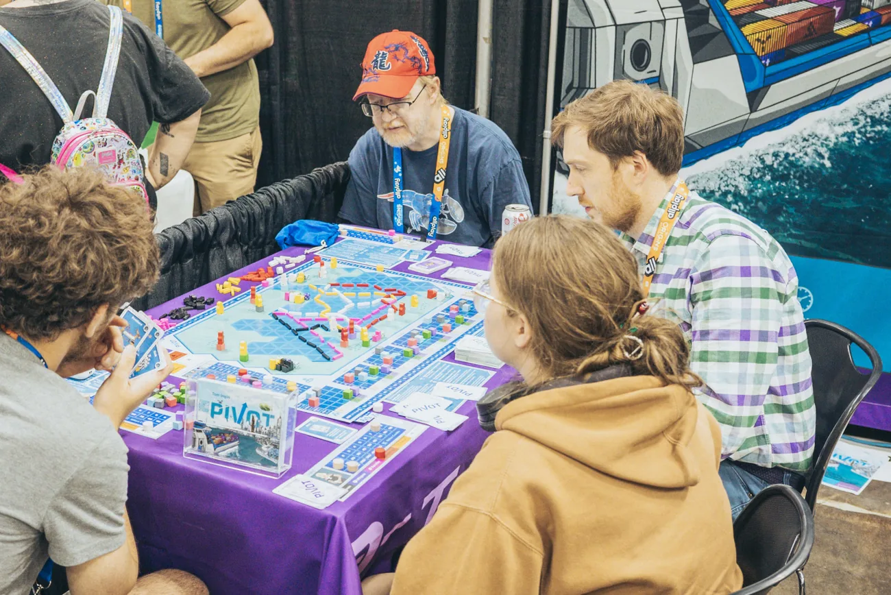 Players around a table mid-game of Pivot at a convention