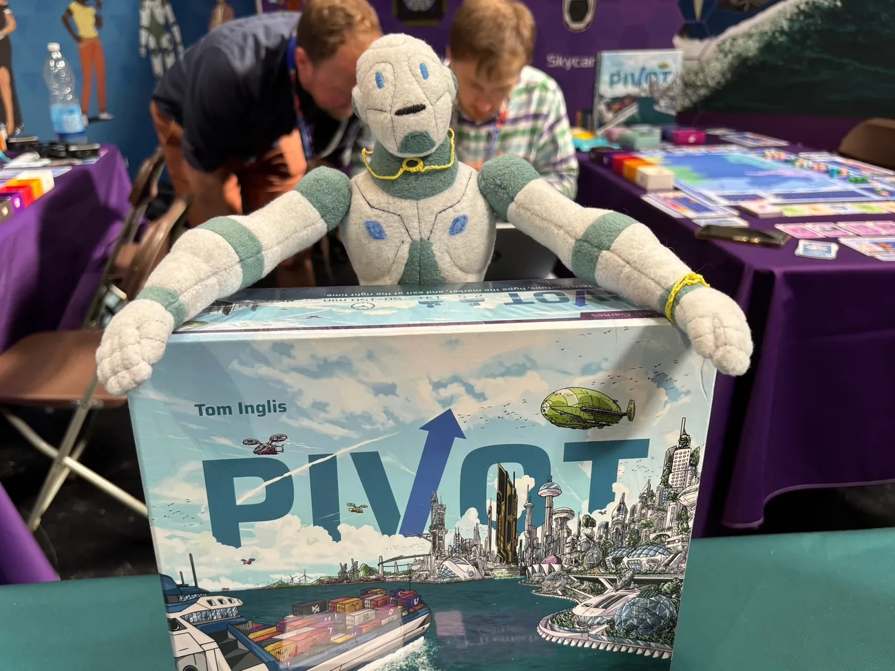 Oscar, the Teòmach robot mascot, draped over a copy of Pivot at UK Games Expo